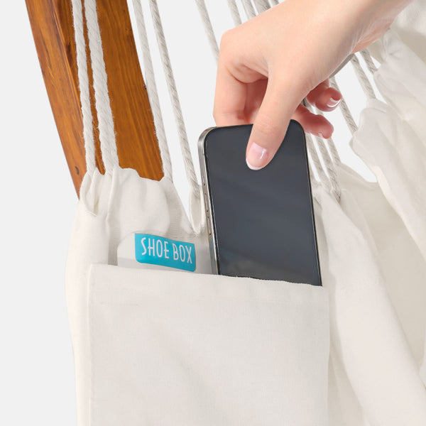 Hand placing a smartphone into a white pouch labeled 'Shoe Box' on a wooden surface.