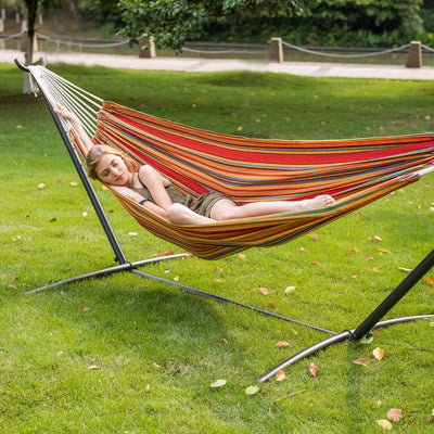 A woman relaxing on Lazy Daze Brazilian Premium Polycotton Hammock in a backyard.#color_red-yellow-stripes