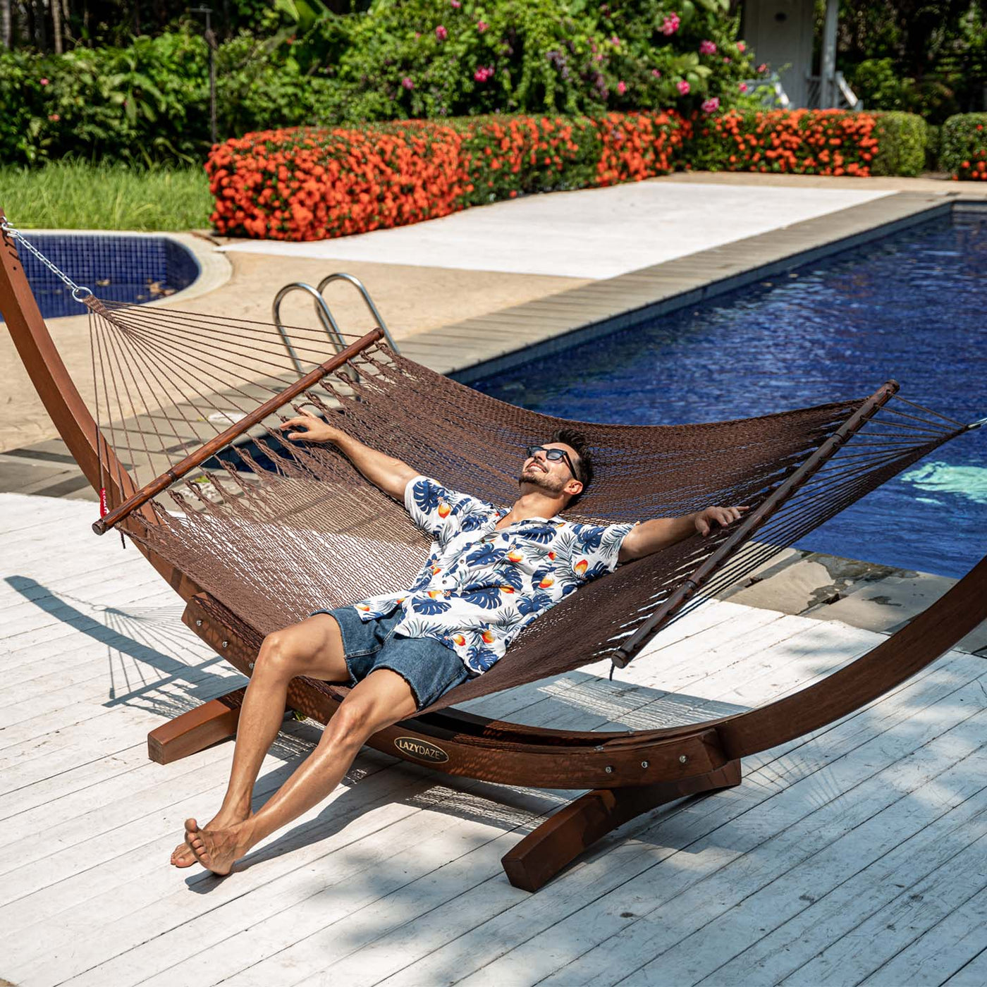 Person relaxing on Lazy Daze Double Caribbean Rope Hammock in Brown by the poolside.#color_brown