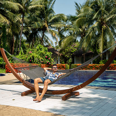 Person relaxing on Lazy Daze Double Caribbean Rope Hammock in Gray by the poolside.#color_gray