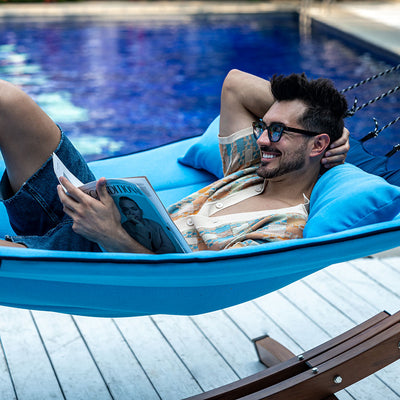 Man enjoying relaxation on Lazy Daze Double Hammock with Curved Spreader Bar in blue by the backyard pool.#color_blue