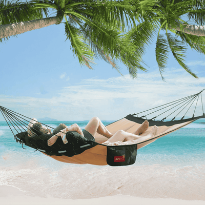 A couple relaxing in the Lazy Daze Double Hammock with Curved Spreader Bar in khaki on a sunny beach.#color_khaki