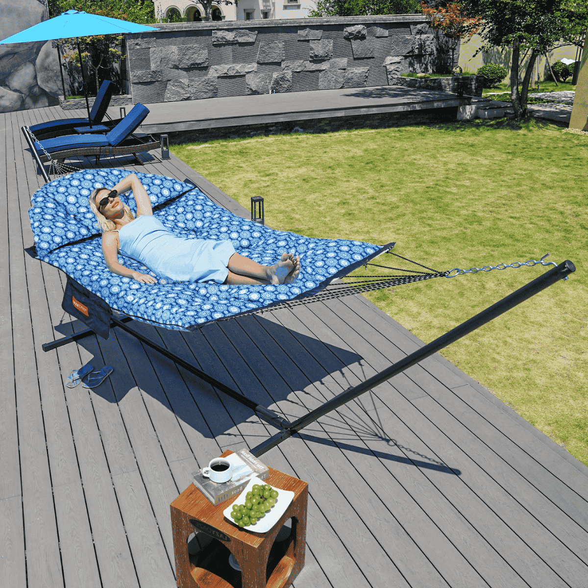 A woman relaxing on the Lazy Daze Double Hammock with Curved Spreader Bar in navy, set up in a backyard.#color_navy