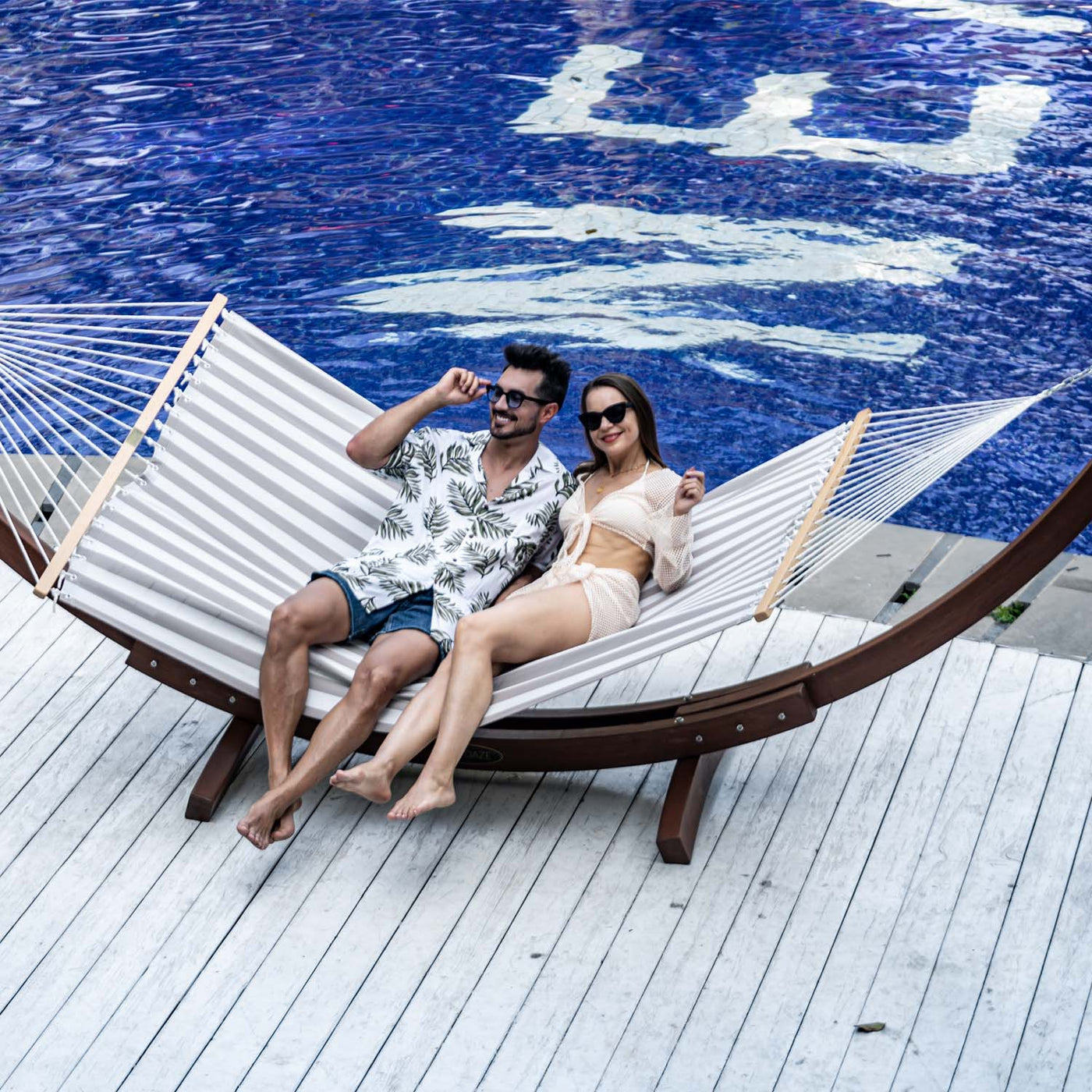 A couple unwinding on the Lazy Daze Double Poolside Hammock in Beige White Stripes beside the pool.#color_beige-white-stripes