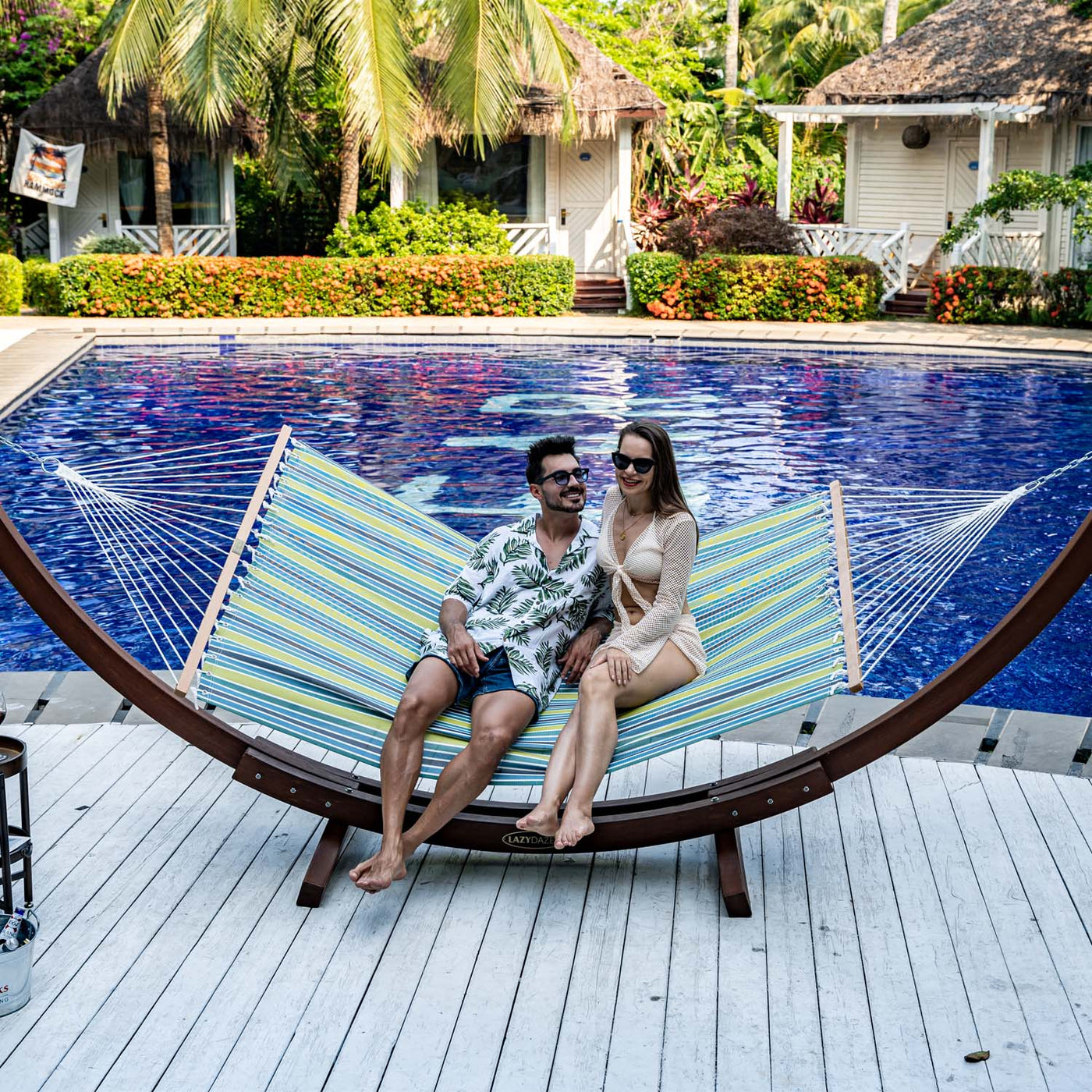 Couple relaxing on Lazy Daze Double Poolside Hammock in Blue Stripes in the backyard.#color_blue-stripes