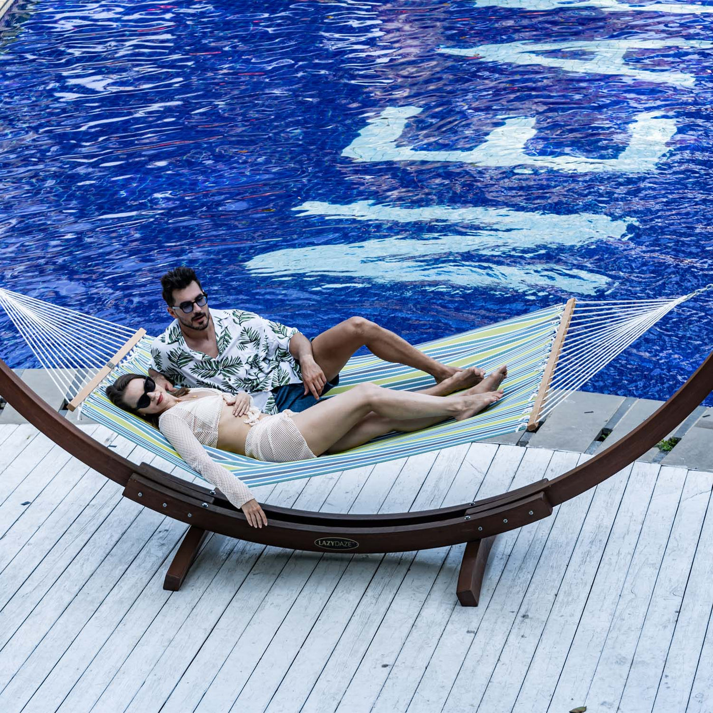 Couple relaxing on Lazy Daze Double Poolside Hammock in Blue Stripes by the poolside.#color_blue-stripes