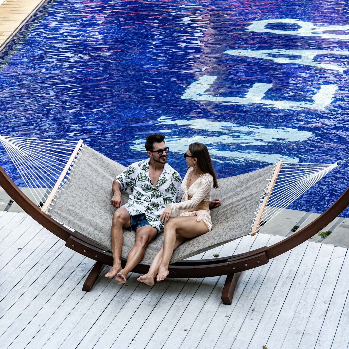 Two people enjoying a leisurely moment on the Lazy Daze Double Poolside Hammock in Vines, beside the pool.#color_vines