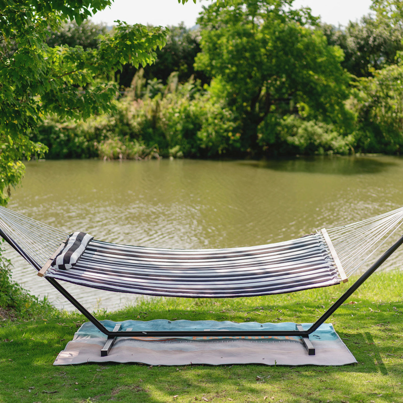 Large Double Quilted Hammock n Black White Stripes showcased near a serene lake on a green lawn.#color_black-white-stripes