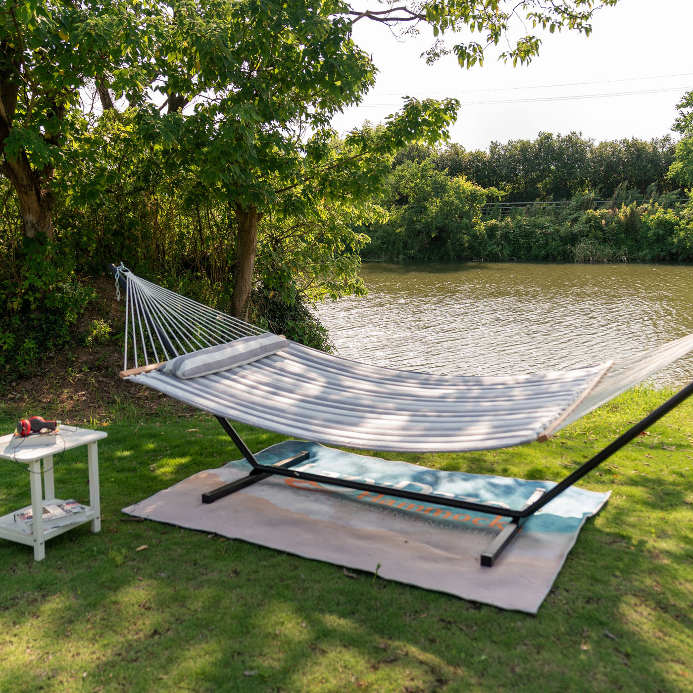 Large Double Quilted Hammock in Gray White Stripes placed near a serene lakeside grassy area.#color_gray-white-stripes