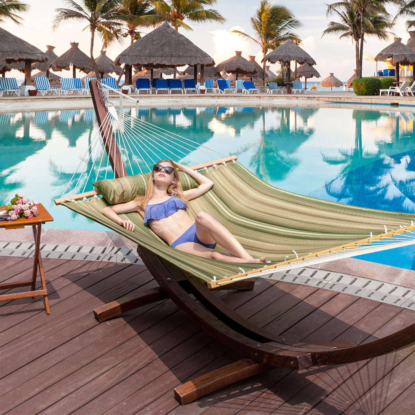 Woman relaxing on the Lazy Daze Large Double Stripes Quilted Hammock by a backyard pool.#color_green-brown-stripes