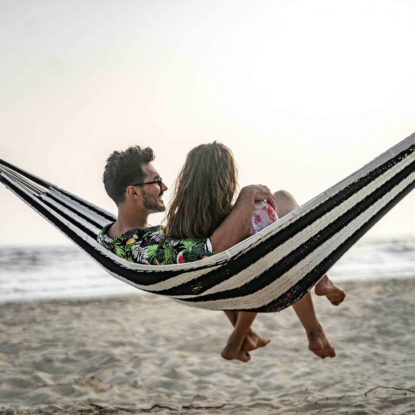 Couple relaxing in the Lazy Daze Mayan Family Hammock in black and white near the ocean.#color_black-and-white-stripes