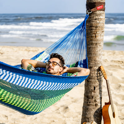 Man unwinding in the Lazy Daze Mayan Family Hammock on the beach.#color_blue-and-green-stripes