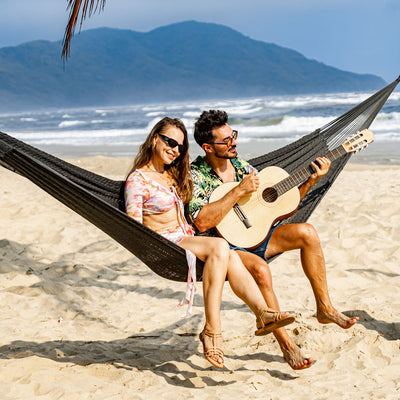 A couple relaxing in the Lazy Daze Mayan Family Hammock in gray on a scenic beach.#color_gray