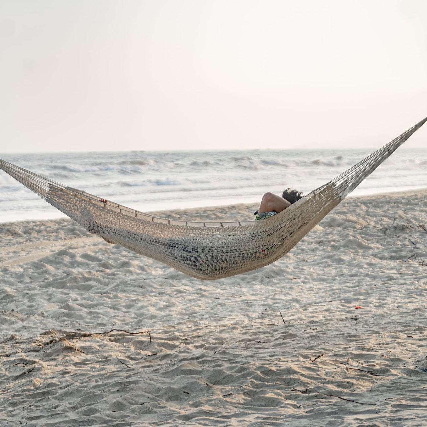 Lazy Daze Mayan Family Hammock in white color with a man relaxing on the beach.#color_white