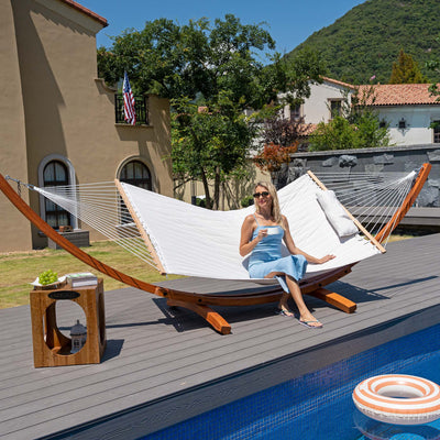 A woman relaxing on the Lazy Daze Sunbrella Double Quilted Hammock in Cream in a peaceful backyard.#color_cream