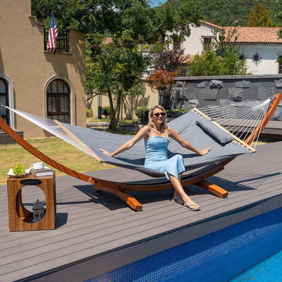 A woman enjoying a moment of relaxation on the Lazy Daze Sunbrella Double Quilted Hammock, placed in a backyard.#color_gray