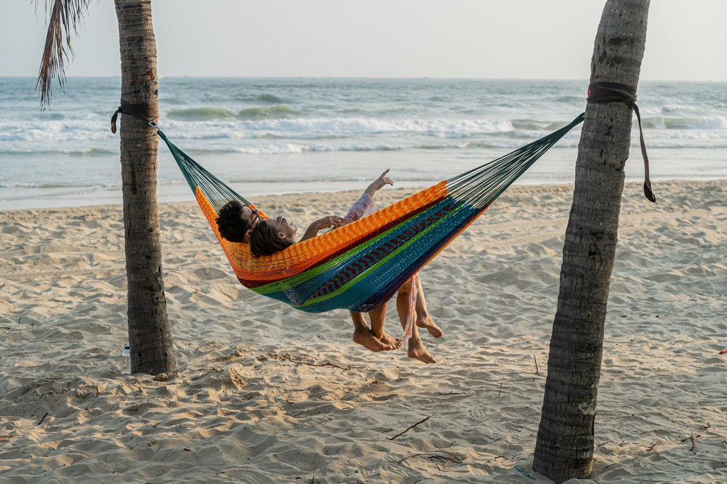 Two person sit on mayan hammock by the beach